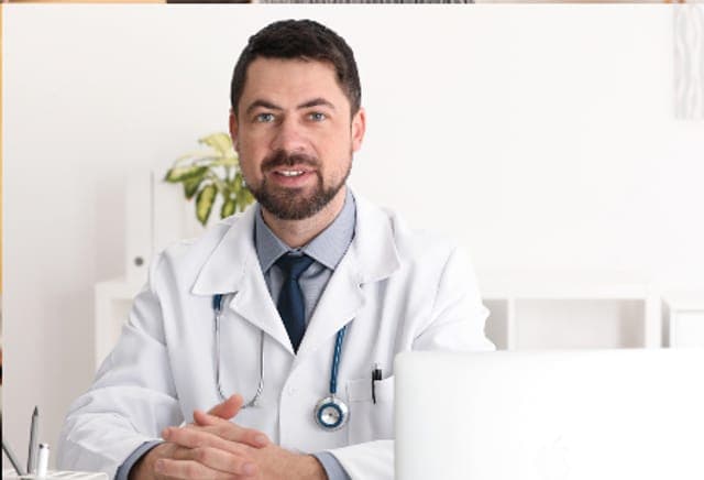 Arbeitsschutz für Praxen und Gesundheitsbetriebe: Arzt mit Stethoskop am Schreibtisch seiner Praxis