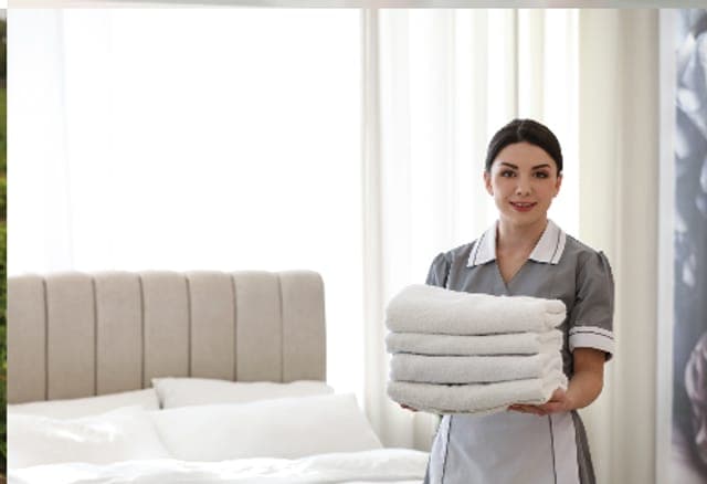 Arbeitsschutz in der Hotellerie: Hausdame mit frischen Handtüchern im Hotelzimmer