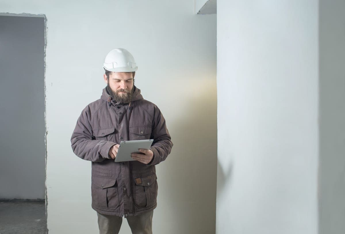 Fachkraft für Arbeitssicherheit anfragen: Fachkraft mit Schutzhelm dokumentiert die Begehung am Tablet
